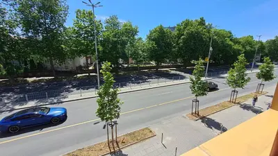 a blue car driving down a street with trees at Studio Demokratsia in Burgas City