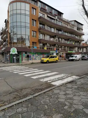 a yellow car driving down a street with a building at Студио Слънчево утро in Burgas City