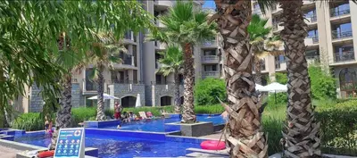 a hotel swimming pool with palm trees in front of a building at Wonderful Deluxe Appartement in Cascadas Family Resort Sunny Beach in Sunny Beach