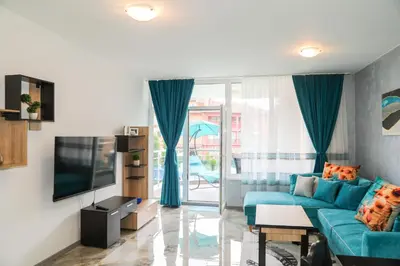 a living room with a blue couch and a tv at Luxury First Line apartment with pool and sea view in complex Oazis in Ravda