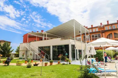 a building with a patio and a lawn with chairs and umbrellas at Luxury First Line apartment with pool and sea view in complex Oazis in Ravda
