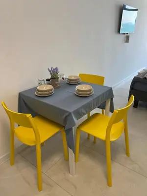 a dining room table with yellow chairs and a table with plates at Aliara Dilara Beach Apartments in Pomorie