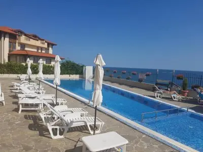 a pool with chairs and umbrellas next to a building at Coral Beach Apartment in Sveti Vlas