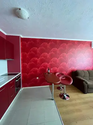 a kitchen with a red wall with a table and two stools at Apart hotel Gallery B in Sunny Beach