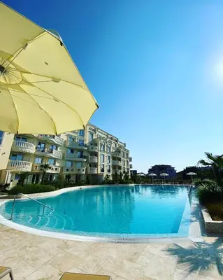 a large swimming pool with an umbrella and some buildings at Ravda Bliss with a pool in Ravda