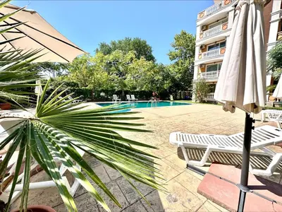 a pool with an umbrella and chairs and a building at Villa Aria - Menada Apartments in Sunny Beach