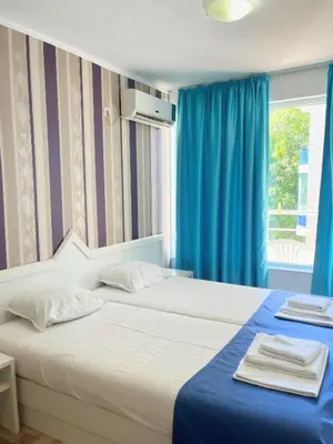 a bedroom with two beds with blue curtains and a window at STELA in Nesebar