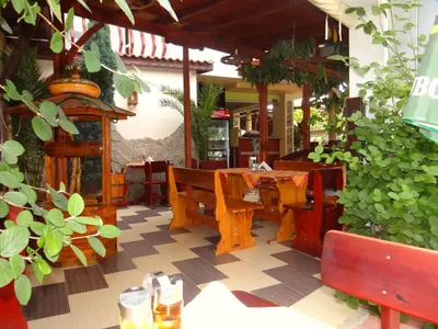 a restaurant with wooden tables and benches and plants at Guest House Rosa in Kiten