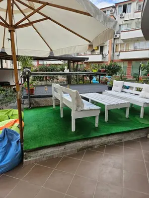 a patio with two white benches and an umbrella at Guest House Petrovi in Ravda