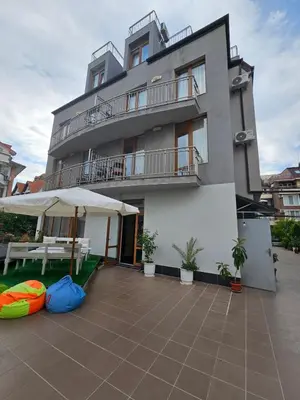 a building with a patio and a table and an umbrella at Guest House Petrovi in Ravda