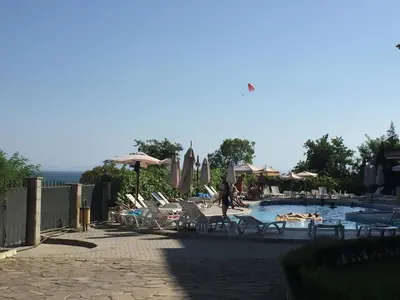 a pool with chairs and umbrellas and a person walking by it at Studio Apartment C32 in Dream Holiday Complex Ravda in Ravda