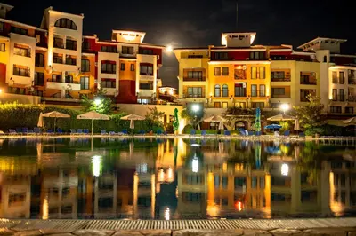 a pool of water in front of buildings at night at Menada Aheloy Apartments in Aheloy