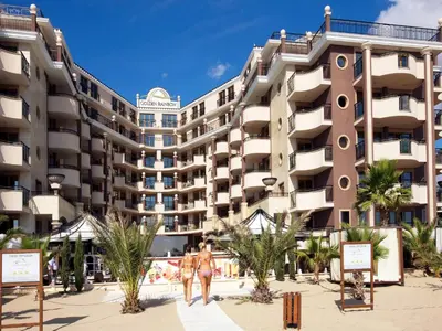 a building on the beach with people walking in front of it at Hotel Golden Ina - All Inclusive - Beachfront in Sunny Beach