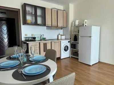 a kitchen with a table and a white refrigerator at Golden Hermes Apartments in Sunny Beach