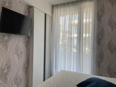 a bedroom with a window and a television on a wall at Сарафово Лукс Тераса Първа Линия in Sarafovo