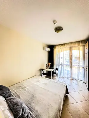 a bedroom with a bed and a table and a window at Студио Каскадас М5 in Sunny Beach
