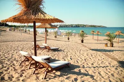 a beach with chairs and a straw umbrella and the ocean at Ваканционна Къща в Greenn Life Созопол in Sozopol
