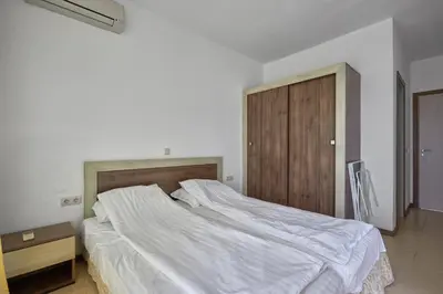 a bedroom with a large white bed and a wooden cabinet at Апартамент на плаж Градина in Chernomorets