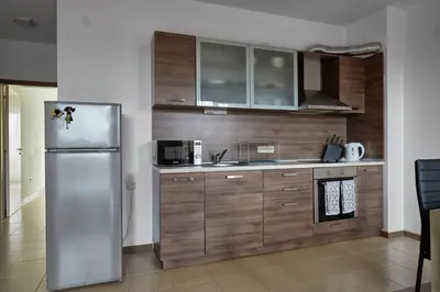 a kitchen with a stainless steel refrigerator and wooden cabinets at Апартамент на плаж Градина in Chernomorets