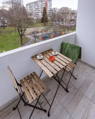 a wooden table and chairs on a balcony with a window at Happy Lazur in Burgas City