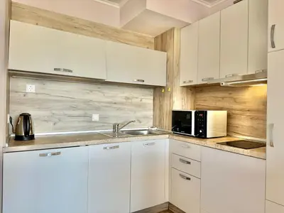 a white kitchen with a sink and a microwave at Sunshine apartment in Shkorpilovtsi