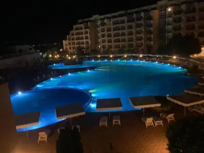 a large blue swimming pool at night with buildings at Midia SP Apartments in Aheloy