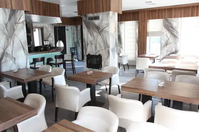 a restaurant with wooden tables and white chairs at Milano Hotel in Burgas City