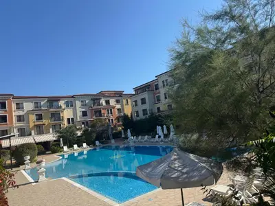 a swimming pool with an umbrella and some buildings at Marteo Apartments 105 - Sozopol in Sozopol