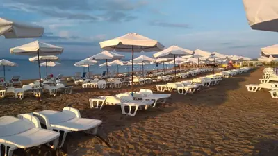 a row of white chairs and umbrellas on a beach at Апартамент МеГи in Burgas City