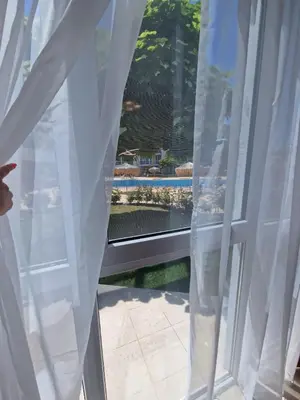 a window with white curtains and a view of a pool at Апартамент МеГи in Burgas City