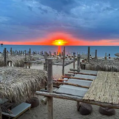 a beach with tables and straw umbrellas and the sunset at Infinity view 2 Shkorpilovci in Shkorpilovtsi