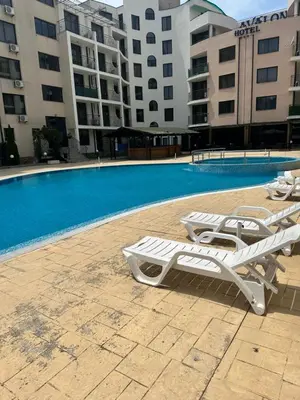 a swimming pool with white lounge chairs next to a building at Apart Hotel Avalon in Sunny Beach
