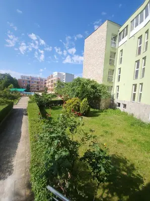 a grassy area next to two buildings with trees at Jolly apartments in Nesebar