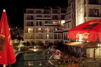 a hotel with a pool and a cocacola umbrella and a building at Rose Village Private Apartment in Sunny Beach