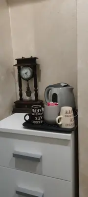 a clock sitting on top of a dresser with a tea kettle and a cup at Aпартамент Жужа in Nesebar