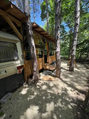a rv parked in the woods next to trees at Каравана градина in Sozopol