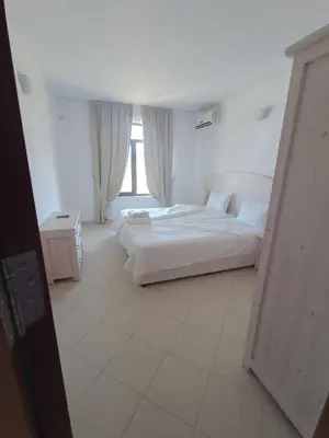a white bedroom with two beds and a window at Oasis Beach 2 bedroom apartment in Lozenets
