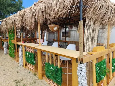 a restaurant with a large wooden table and a thatched roof at Къмпинг Европа Юг in Burgas City