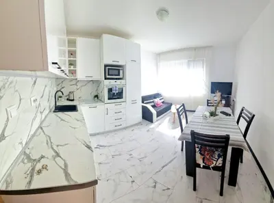 a kitchen with white cabinets and a table with chairs at Апартамент Бижу М in Pomorie