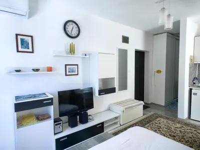a white living room with a television and a clock on the wall at Blu Bey Pomorie in Pomorie