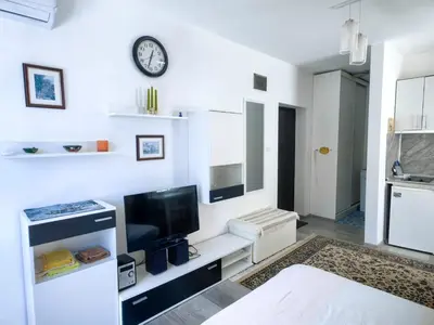 a white living room with a television and a clock on the wall at Blu Bey Pomorie in Pomorie