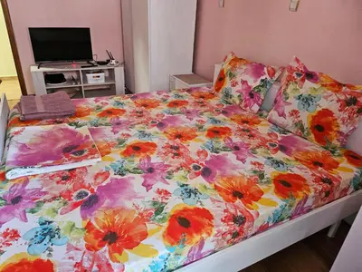 a bed with a floral comforter and a television at Стая за гости на Бургас 1 in Burgas City