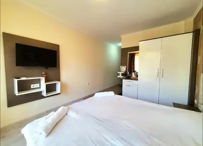 a bedroom with a large white bed with a tv on the wall at Уютно студио до морето - апартаменти 25 и 26, топ локация - Cozy Studio by the Sea - Apartments 25 and 26 Top Location in Sveti Vlas