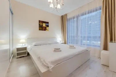 a white bedroom with a bed and a large window at АТ apartment - Pool View in Varna City