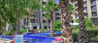 a hotel swimming pool with palm trees in front of a building at Luxury Apartment in Cascadas Family Resort Sunny Beach in Sunny Beach