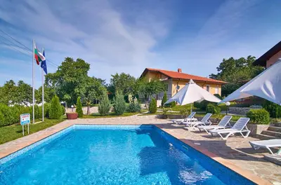 a swimming pool with chairs and umbrellas next to a house at BulgariaVilla - Royal Villas in Bryastovets