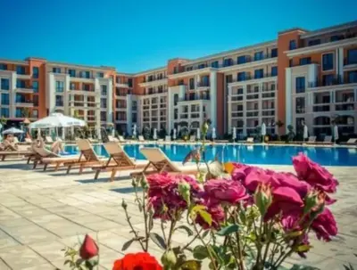 a pool with chairs and flowers in front of a building at Prestige Fort Beach - Menada Apartments in Sveti Vlas