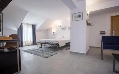 a white bedroom with a bed and a blue chair at Hotel Mistral in Nesebar