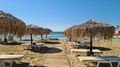 a beach with tables and straw umbrellas and the ocean at Apartament w Bułgarii in Sveti Vlas