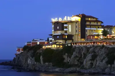 a building on a cliff near the ocean at night at Hotel Parnasse in Sozopol